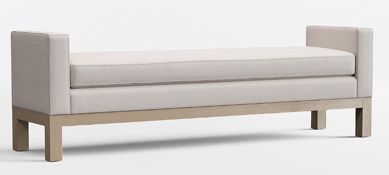 A contemporary upholstered bench with rectangular block arms and an exposed wooden base. The bench features a single, thick, removable seat cushion and an upholstered deck, all in a light, neutral-toned fabric. The wooden frame has a light, possibly washed or natural finish, forming a sturdy base with square legs. — 3D model