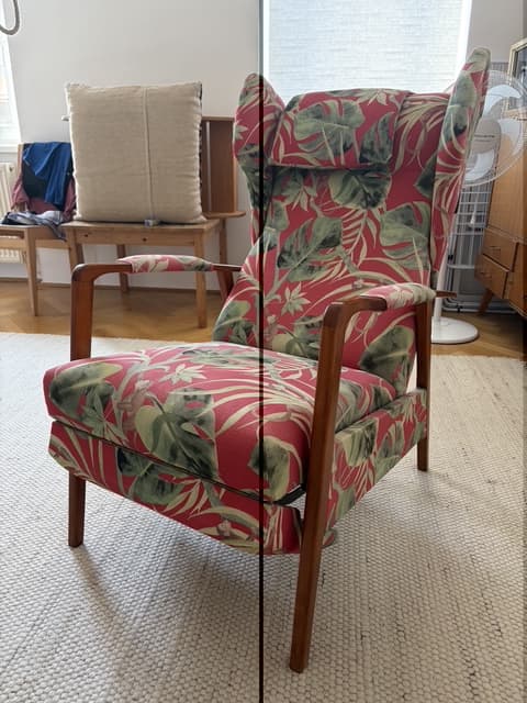 A high-back armchair featuring a vibrant tropical print upholstery and an exposed dark wood frame. The chair has a classic wingback design with a separate headrest cushion and straight, tapered legs. — 3D model