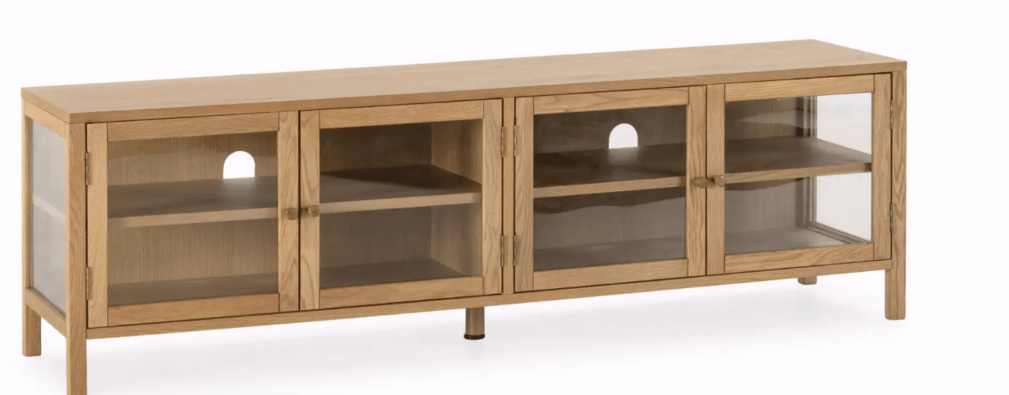 A modern, long, and low media console constructed from natural light-colored oak wood, featuring a clean, minimalist design. It includes four compartments, each accessible via a hinged clear glass door with small wooden knob handles. The two central compartments have circular cutouts on their back panels for cable management, indicating its function for electronic devices. The unit is supported by short, subtly recessed legs. — 3D model