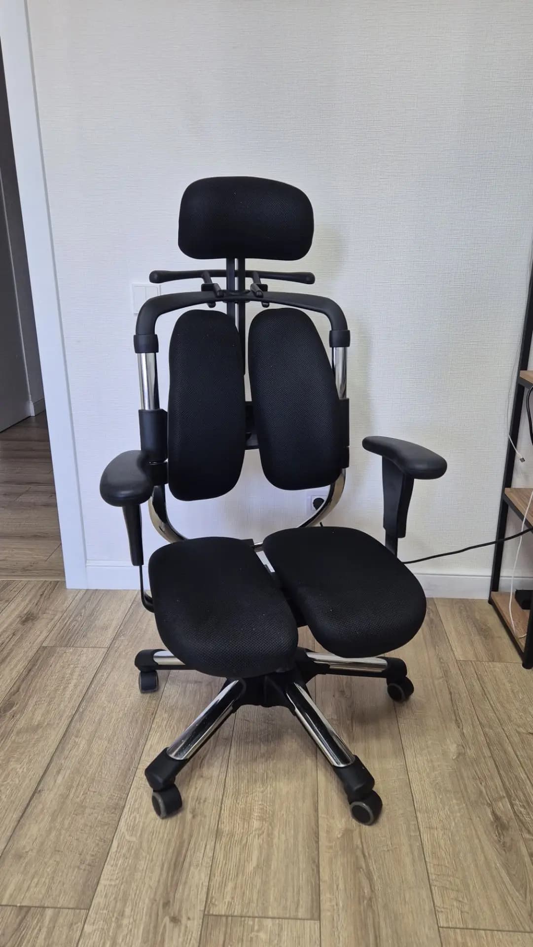 An ergonomic office chair featuring a unique split backrest and bifurcated seat, both upholstered in black fabric. It has a contoured headrest, adjustable armrests, and a polished metal five-star base with casters. — 3D model