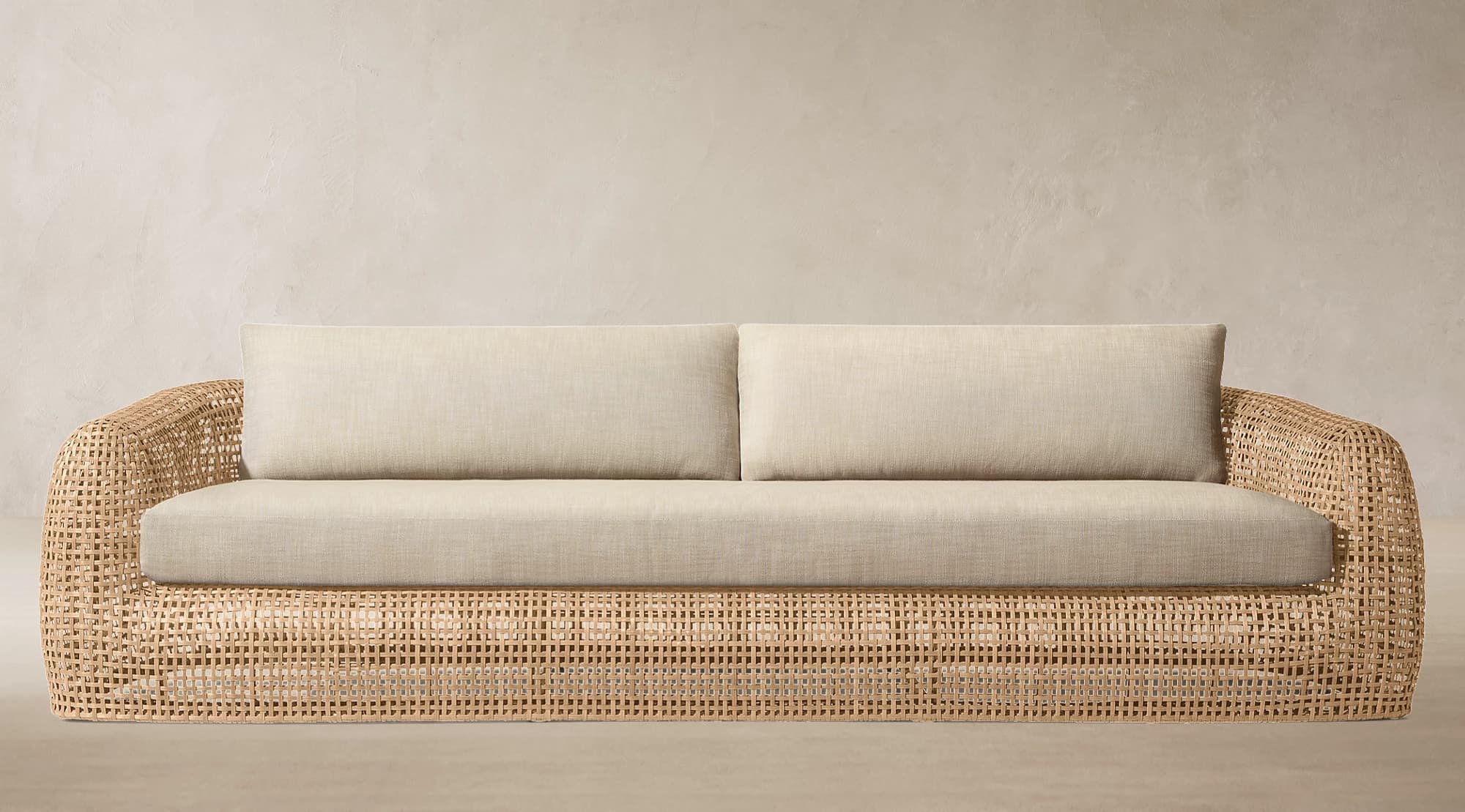 A contemporary sofa featuring a curved, open-weave rattan frame and soft, light-colored upholstered cushions on the seat and back. — 3D model