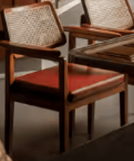 A contemporary armchair featuring a solid dark wood frame, a caned backrest, and a red upholstered seat cushion. — 3D model