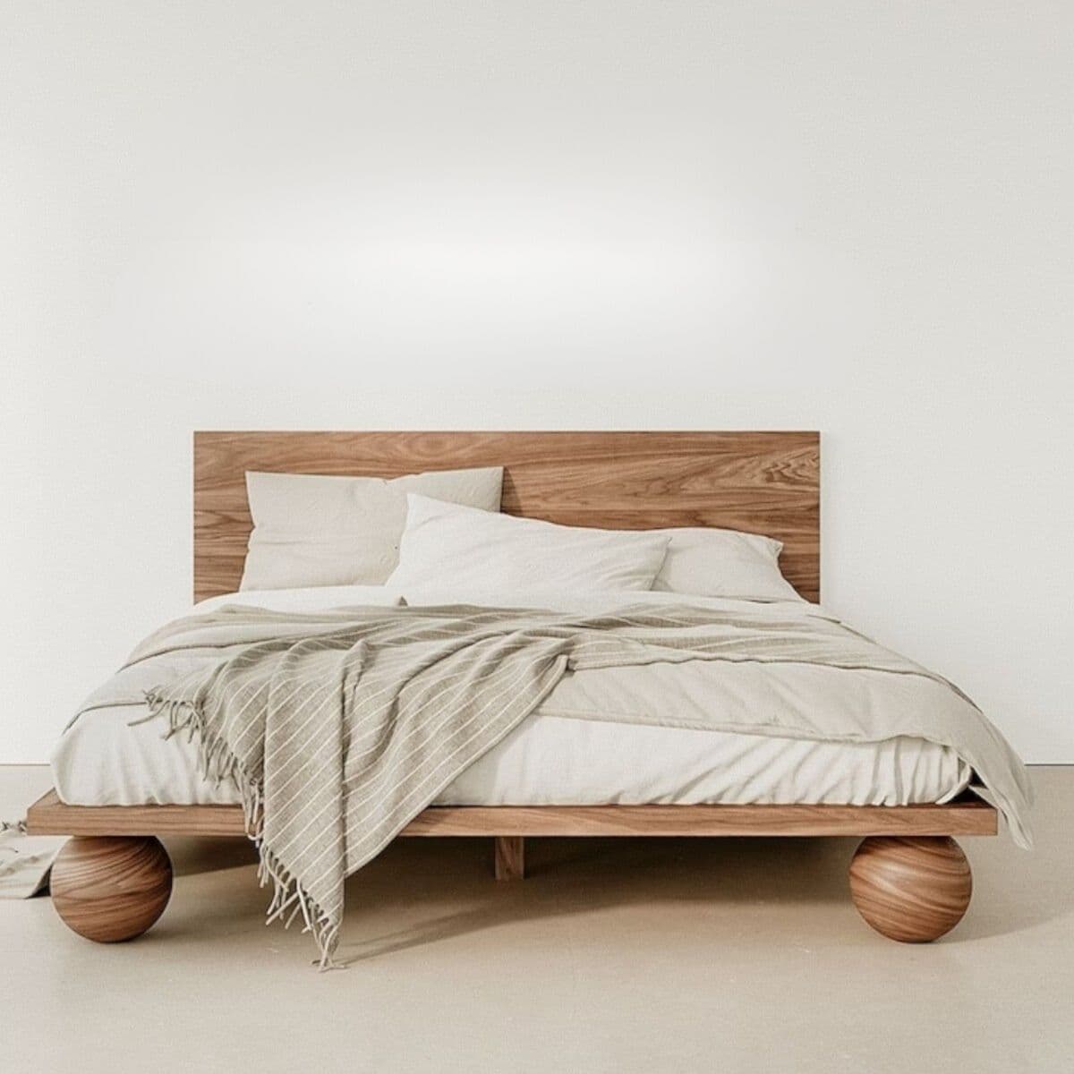 A contemporary wooden bed frame with a minimalist design. It features a solid wood headboard that is wider than the frame and rests directly on the floor. The bed frame itself is low to the ground and supported by two large, spherical wooden legs at the head and two smaller rectangular legs at the foot, creating a visually striking and unique silhouette. The bed is dressed with white linens and a striped throw blanket. — 3D model