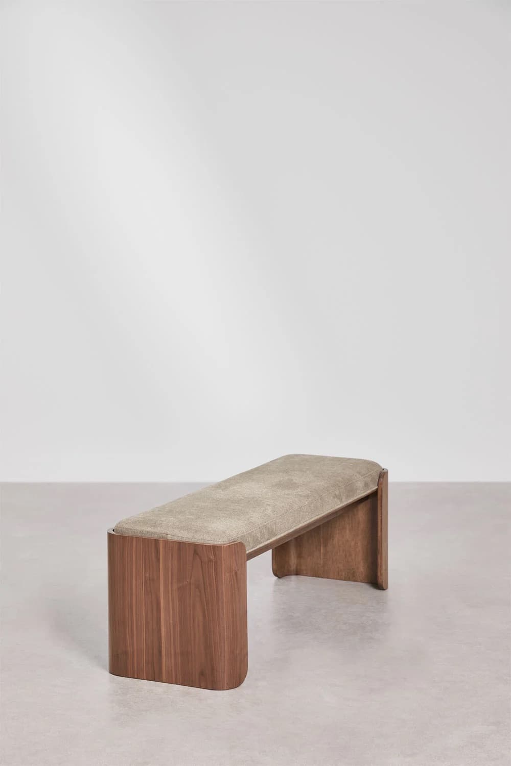 A modern upholstered bench with a wooden base. The bench features a gently sloped seat upholstered in a textured beige fabric. The base is constructed from solid wood, likely walnut, with a warm brown finish. The legs have a curved, sculptural design that forms an open structure beneath the seat. The overall aesthetic is minimalist and elegant. — 3D model