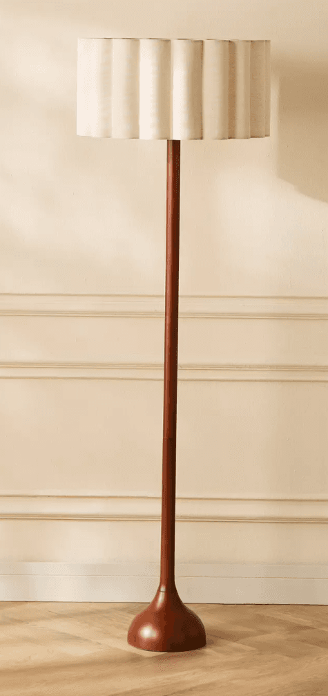 A tall, slender floor lamp featuring a dark wooden base and stem, complemented by an off-white, pleated fabric shade with a distinctive scalloped top rim. — 3D model