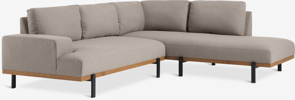A sectional sofa with a light beige fabric upholstery. It features a modular design with a chaise lounge on one end and an armrest on the other. The frame is visible and appears to be made of wood with black metal legs. The back cushions are loose and rectangular. — 3D model