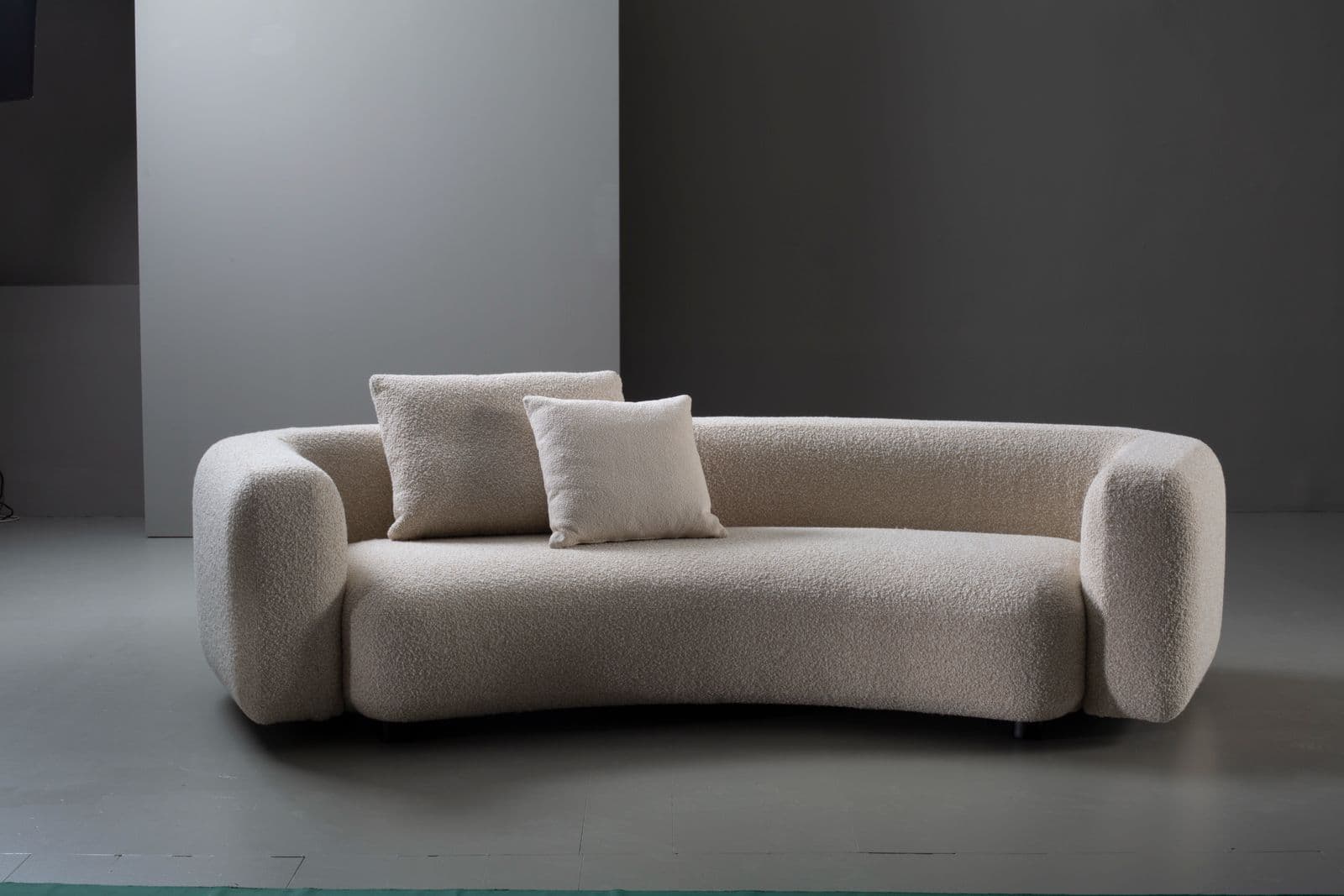A contemporary, low-profile sofa upholstered in a cream-colored boucle fabric, featuring soft, rounded edges and a subtly curvilinear form, accompanied by two matching throw pillows. — 3D model