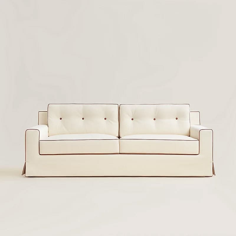 A white sofa with tufted back cushions and contrasting dark piping along the edges of the cushions and arms. The sofa features a skirted base and a clean, modern design. — 3D model