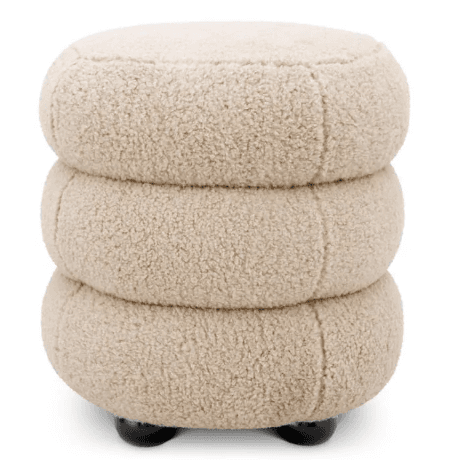 A light beige, plush ottoman featuring a unique stacked design composed of three rounded, tiered segments. It is upholstered in a textured bouclé fabric and rests on small, dark, spherical feet. — 3D model