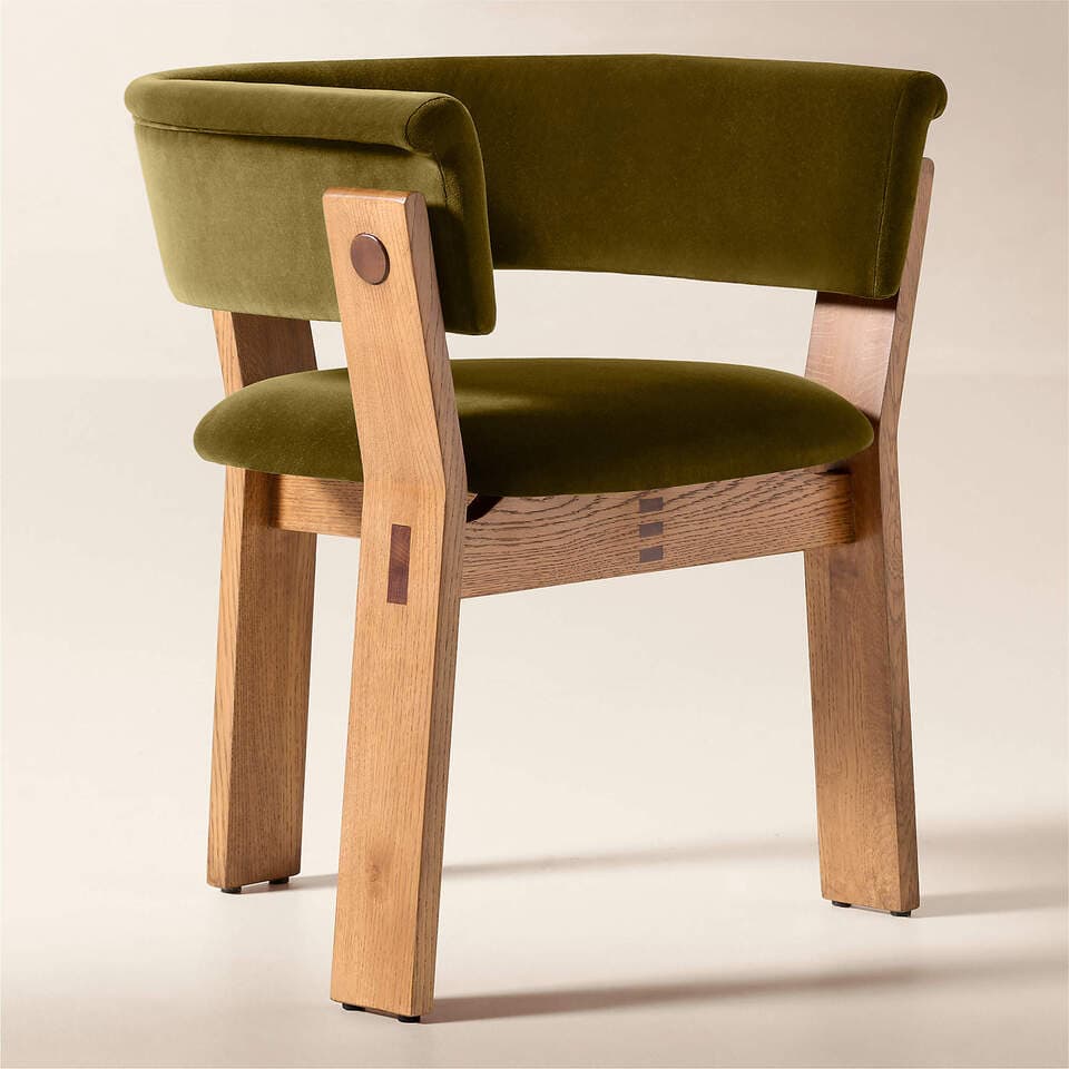 A sturdy, craftsman-style armchair featuring a robust natural oak frame and plush olive green velvet upholstery. The chair showcases prominent exposed joinery details, including through-tenons with darker wood inserts on the legs and decorative splines on the stretcher. The backrest and armrests form a continuous, gently curved line, providing a comfortable embrace. The solid, block-like wooden legs provide strong support, and the overall design emphasizes natural materials and visible construction. — 3D model