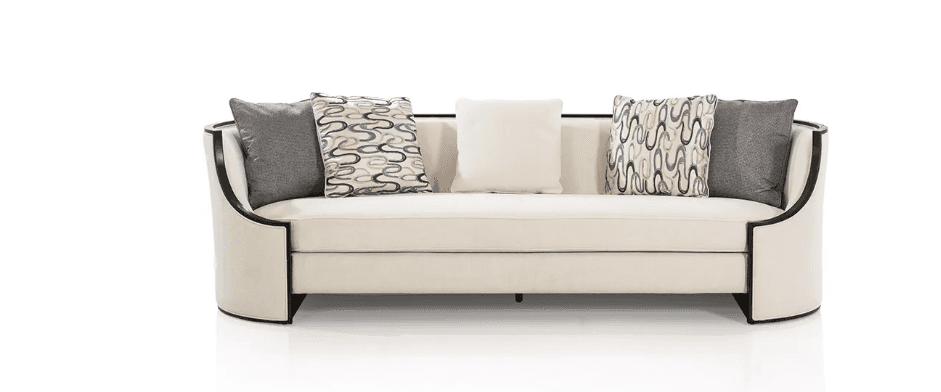 A contemporary three-seater sofa upholstered in light cream-colored fabric, featuring gently curved arms and an exposed dark wood frame. The sofa includes loose seat cushions and an assortment of throw pillows in solid cream, solid grey, and a grey/black abstract patterned fabric. The design emphasizes clean lines and a refined silhouette. — 3D model