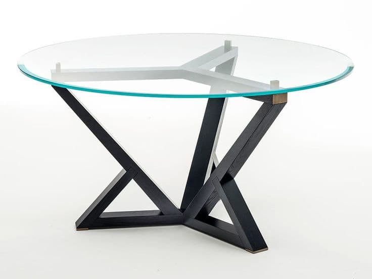 A round dining table featuring a clear glass tabletop and a distinctive geometric base. The base is constructed from dark-finished wood, possibly oak, with an intersecting crisscross design. Metal accents appear at the connection points of the base and possibly supporting the glass. — 3D model
