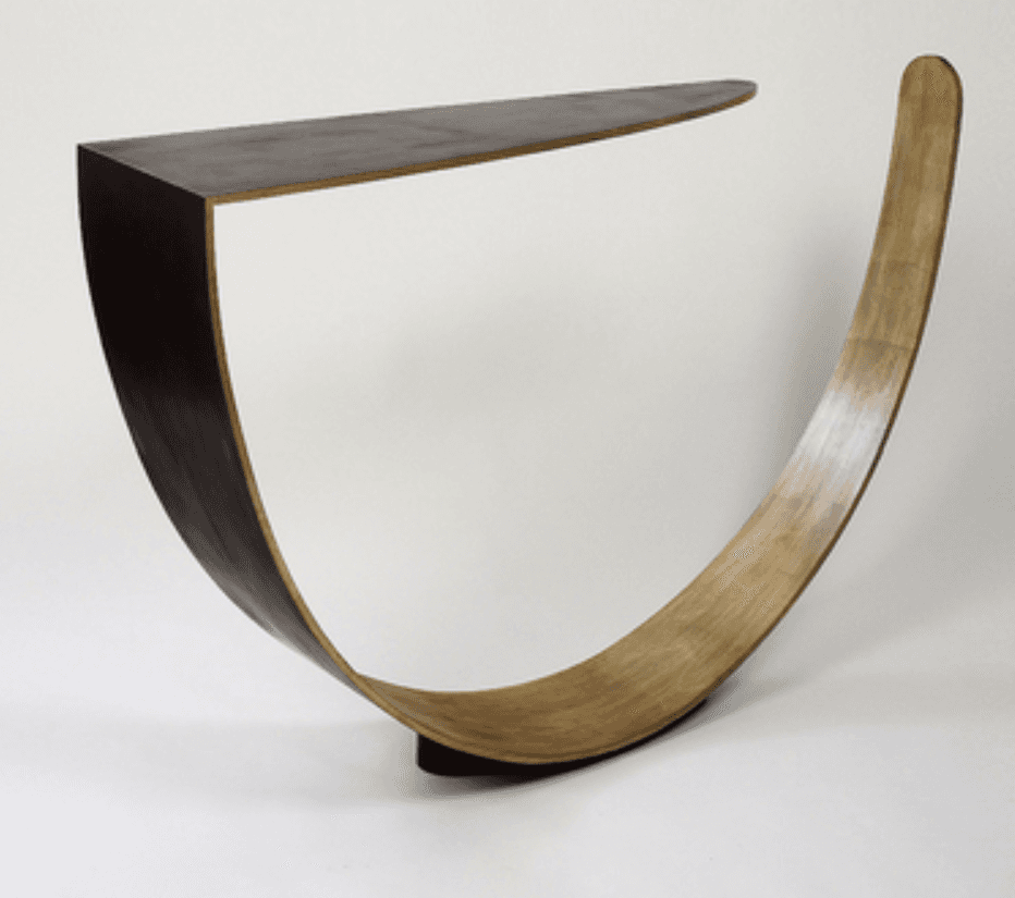 A modern and sculptural console table featuring a unique, dynamic design. It consists of a dark, triangular tabletop with an angled front edge, supported by a sweeping, curved base made of lighter-toned bent plywood. The base forms a graceful arc, with one end connecting to the underside of the dark top and the other end curving upwards, creating an open, airy aesthetic. The overall design emphasizes clean lines, fluid forms, and a striking visual balance. — 3D model