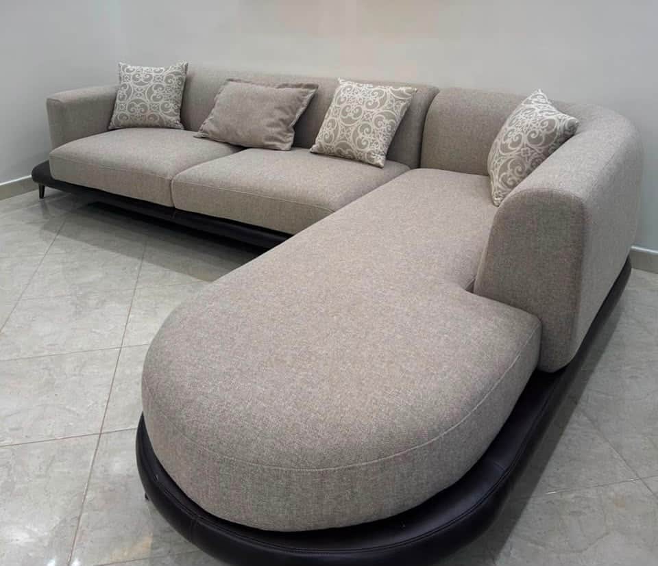 An L-shaped contemporary sectional sofa featuring light greige fabric upholstery, a distinctive roun… — 3D model