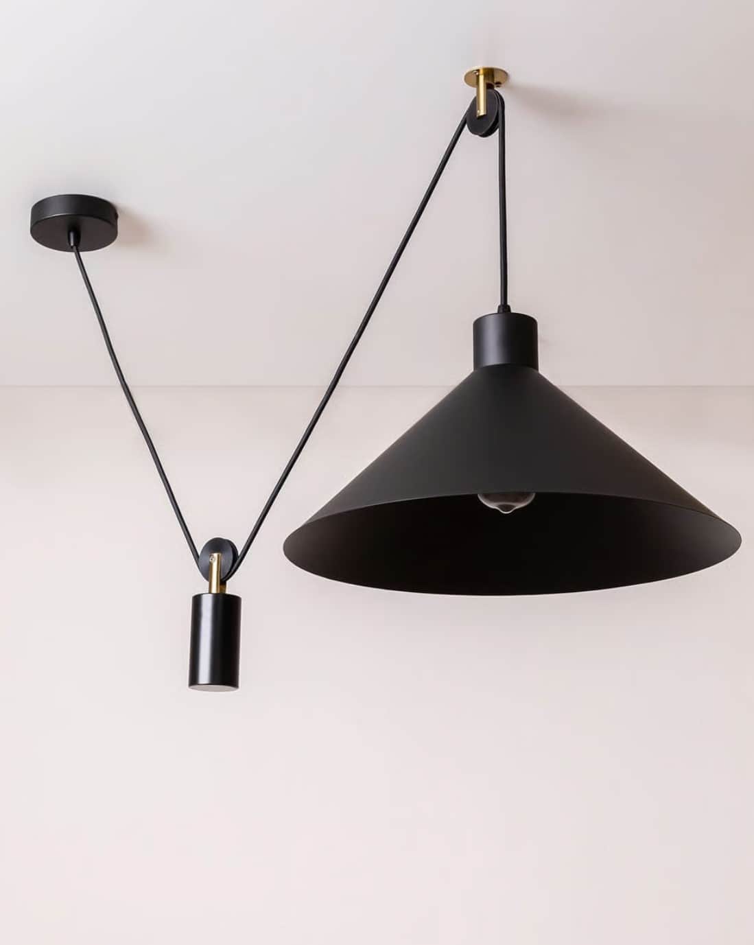 A black conical pendant light featuring an adjustable suspension system with brass-accented pulleys… — 3D model