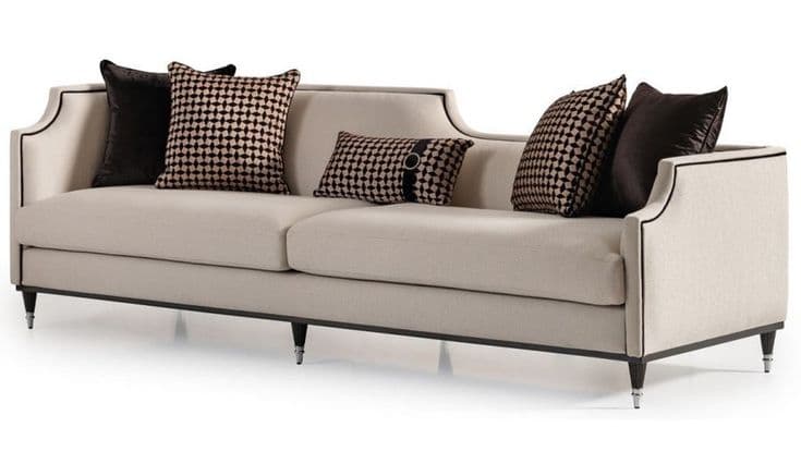 A contemporary three-seater sofa featuring a clean, rectilinear form with subtly curved armrests and a slightly rolled backrest, all outlined with contrasting dark piping. The sofa is upholstered in a light beige fabric and stands on dark, tapered legs with metallic tips. It includes two large seat cushions and several decorative throw pillows in black and patterned brown/beige. — 3D model