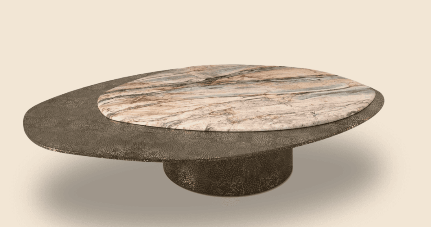 A distinctive coffee table featuring a textured, dark metallic base with an organically shaped, flattened oval profile. Perched atop this base is a round top made of natural stone with prominent veining in shades of pink, beige, grey, and subtle green. The two surfaces are offset, with the round stone top partially overlapping the metallic base, creating a layered visual effect. — 3D model