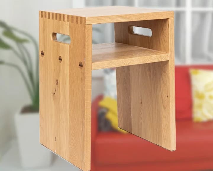 A minimalist wooden stool with a two-tiered design. The stool features a top surface and a lower shelf, supported by vertical panels on the sides. Each side panel has a cut-out handle for portability. The joinery at the top of the side panels is visible, showcasing finger joints. The wood grain is prominent, indicating a natural finish. — 3D model