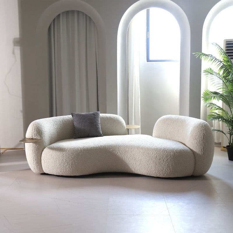 An off-white, intricately curved chaise lounge, upholstered in a textured boucle fabric. The design features an organic, asymmetric shape, with a higher backrest on one end and a lower, more open side on the other. Two small, round, bronze-toned integrated side tables or trays are set into the frame. A single small, patterned cushion rests on the chaise. — 3D model