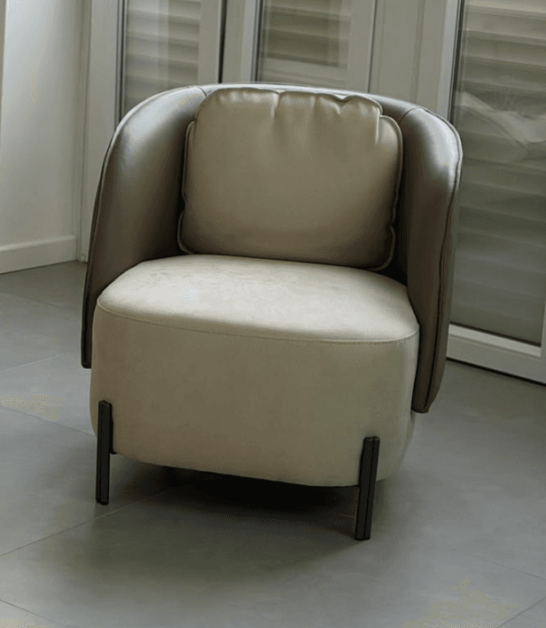 An upholstered tub-style accent chair featuring a two-tone design with a rounded back and integrated armrests. The outer shell is a darker brown, while the inner seat and separate back cushion are a lighter beige or tan. The chair is supported by four slender, angled black metal legs. — 3D model