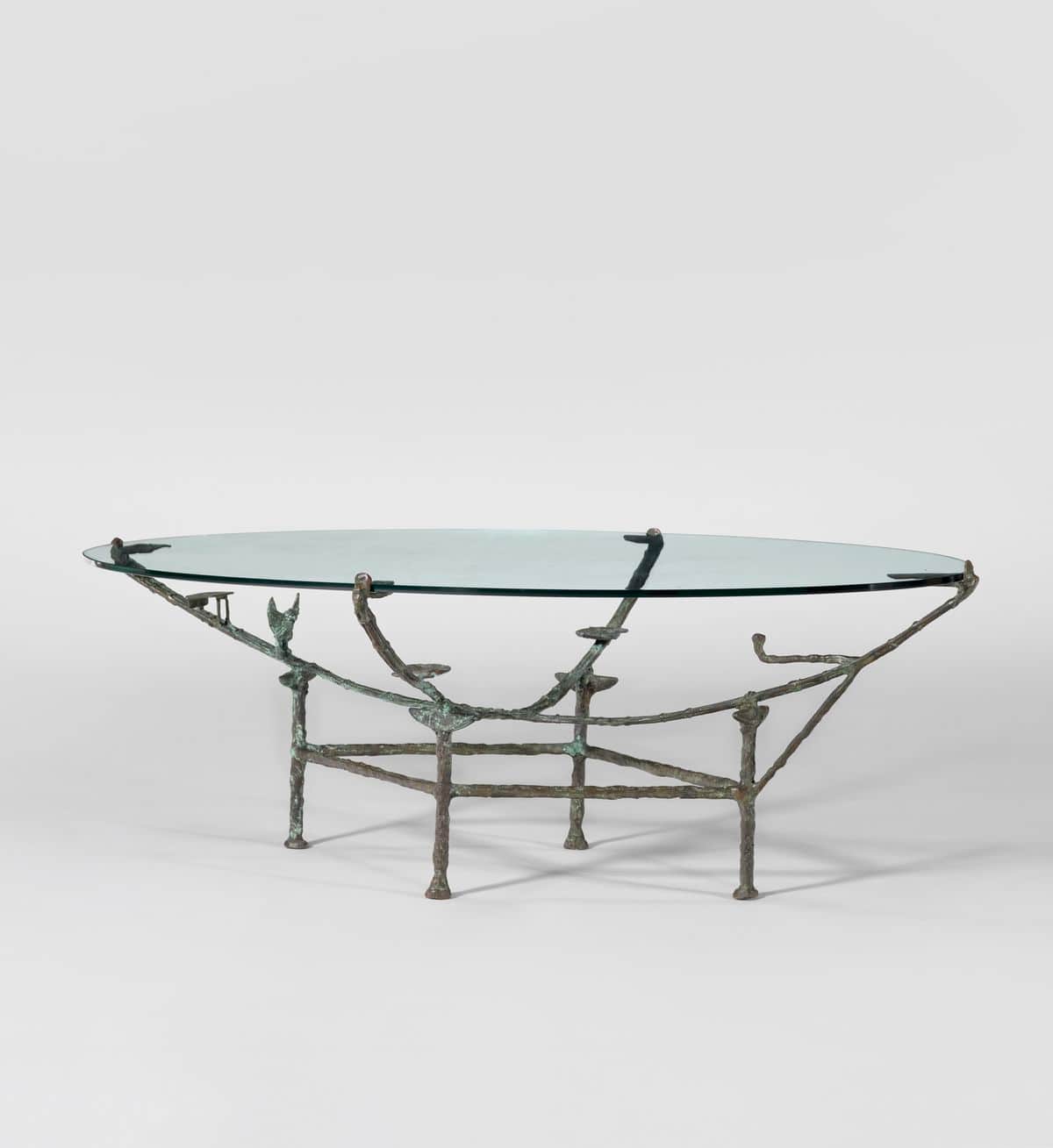 An oval coffee table with a clear glass top supported by a sculptural metal base. The base appears t… — 3D model