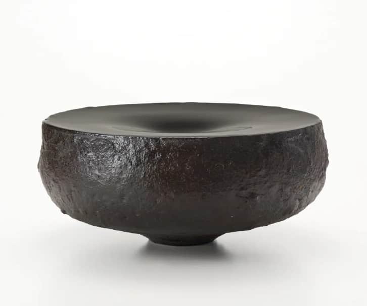 A low, wide, sculptural object resembling a bowl, featuring a rough, dark, textured exterior and a s… — 3D model
