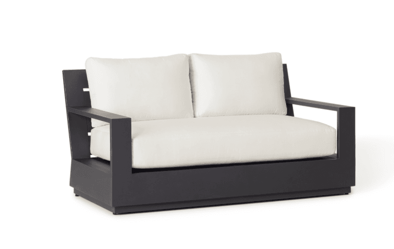 A modern two-seater outdoor loveseat featuring a dark grey, powder-coated metal frame with a clean, linear design. It is fitted with thick, cream-colored upholstered cushions on both the seat and back, providing comfortable seating. The frame has a low profile and solid, rectangular armrests, with subtle horizontal slat detailing on the backrests. — 3D model