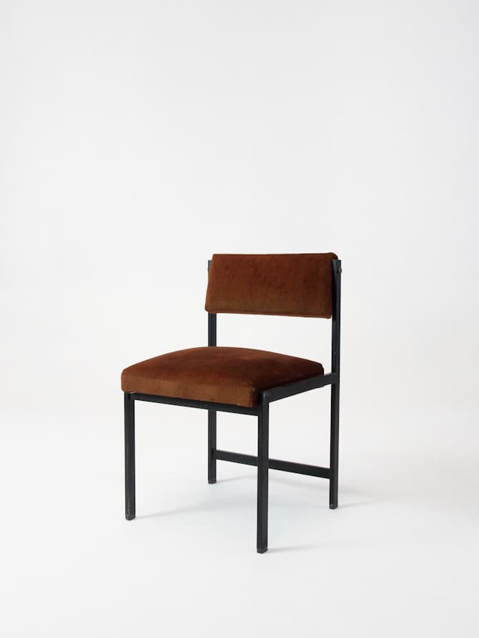 A minimalist accent chair with a dark metal frame and upholstered seat and backrest. The frame has a simple, geometric construction with straight lines. The seat and backrest are covered in a rich, brown velvet-like fabric. — 3D model