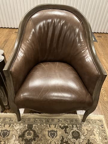A traditional-style accent armchair featuring a curved barrel back and armrests, upholstered in dark brown leather, with an exposed, distressed wooden frame and subtly curved legs. — 3D model