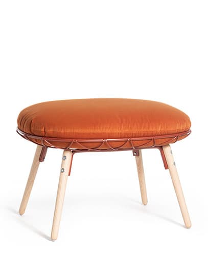 A contemporary round ottoman featuring a plush, burnt orange upholstered cushion. The cushion is cradled within a reddish-brown, open-weave metal wire frame. The frame is supported by four splayed and tapered legs made from light-toned wood, attached with visible metal hardware. The overall design is modern and inviting. — 3D model
