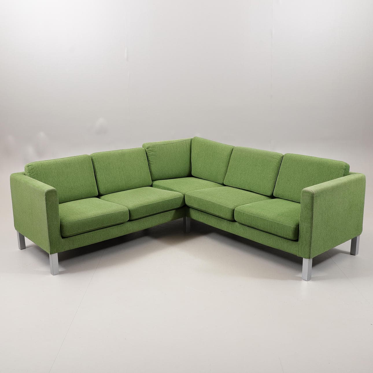 A modern L-shaped sectional sofa upholstered in a textured green fabric, featuring distinct seat and back cushions, track arms, and exposed square-profile silver-toned metal legs. The sofa is composed of two interconnected sections forming a right-angle configuration. — 3D model