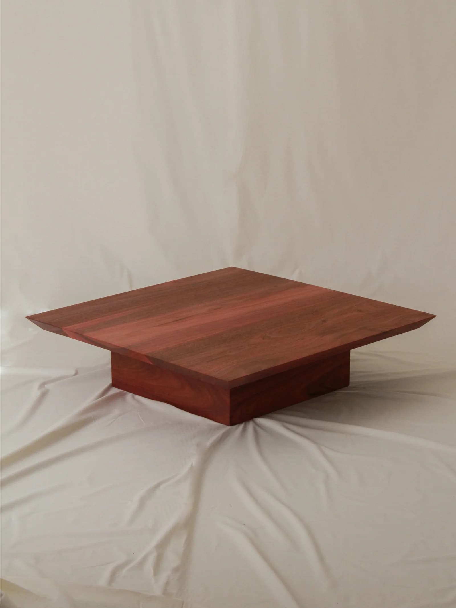 A modern, square-shaped coffee table crafted from reddish-brown wood, featuring a thick tabletop that appears to float above a substantial, square pedestal base. — 3D model