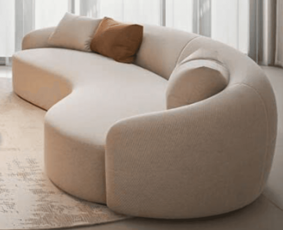 An S-shaped, curvilinear sofa upholstered in a light beige fabric, featuring soft, rounded edges and an integrated backrest/armrest design. It comes with two accent cushions, one light beige and one brown, complementing its neutral color palette. — 3D model