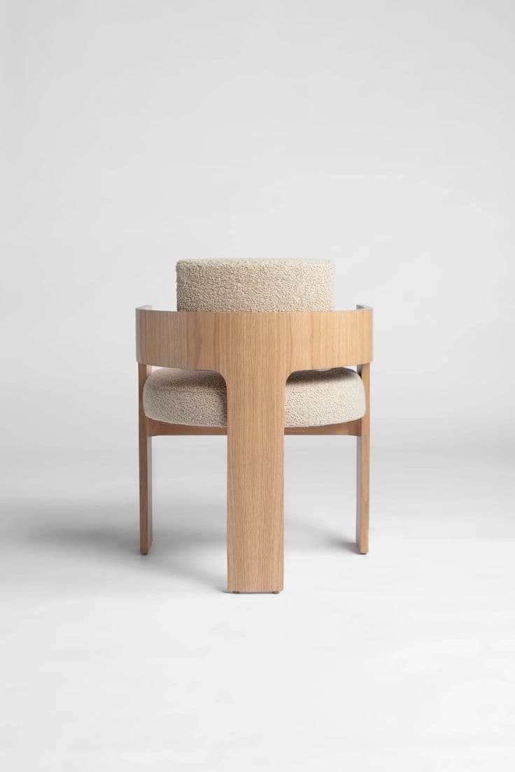 A modern accent chair featuring a distinctive T-shaped oak wood frame and integrated curved backrest/armrests, upholstered with cream bouclé fabric cushions. — 3D model