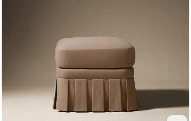 A square, upholstered ottoman featuring a plush top cushion and a continuous box-pleated fabric skirt around its base, all in a neutral beige color. — 3D model