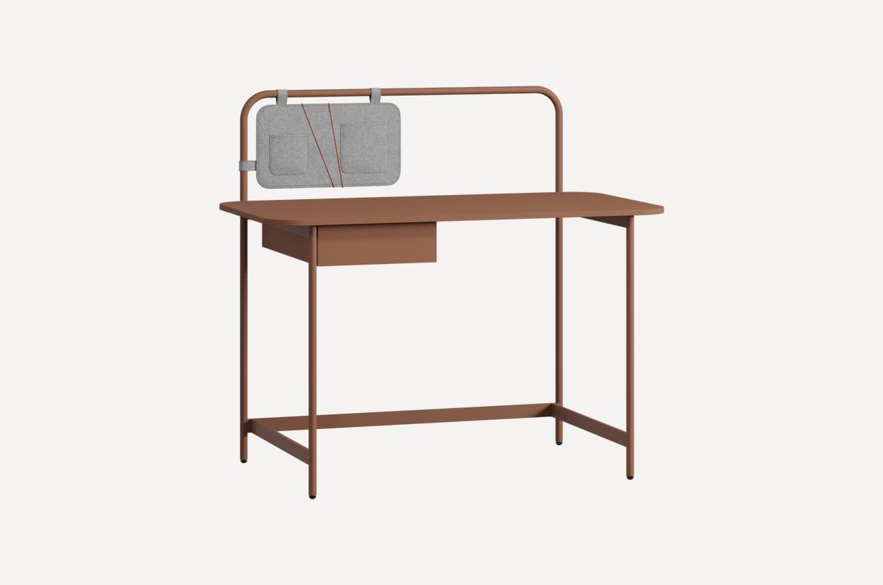 A contemporary desk featuring a monochromatic terracotta finish, constructed with a tubular metal frame. It includes an integrated storage drawer and a raised upper rail, which supports a detachable grey felt organizer panel with pockets and elastic straps. — 3D model