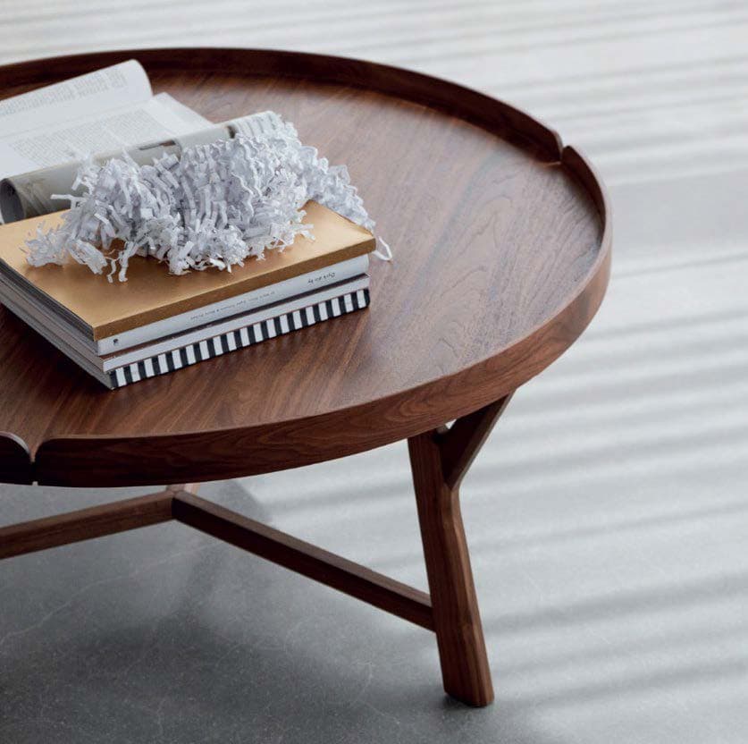 A modern round coffee table featuring a distinctive tray-style top and three splayed wooden legs, finished in a dark walnut tone. The top has a subtle raised edge, giving it a tray appearance, with small cutouts where the legs connect. The overall design is minimalist and contemporary. — 3D model