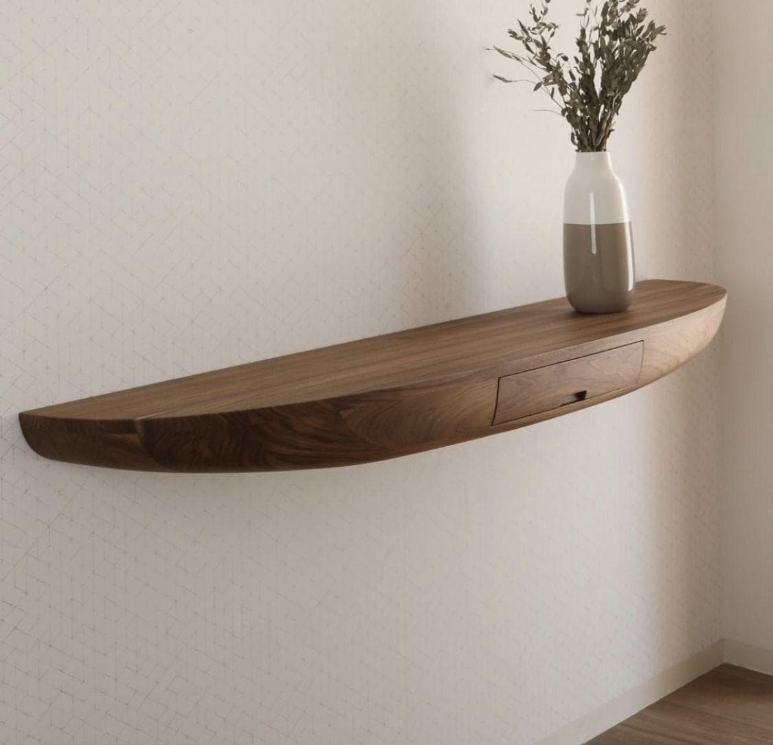 A minimalist, semi-circular floating console table crafted from dark walnut wood. The table features a smooth, polished surface and a gracefully curved front edge. An integrated drawer with a subtle finger pull is seamlessly incorporated into the front face, maintaining the clean lines of the design. The piece is designed to be wall-mounted, providing a space-saving and modern aesthetic. — 3D model