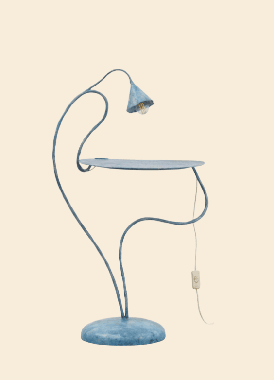 A unique sculptural floor lamp featuring an integrated circular side table. The lamp is crafted from metal with a distressed, muted blue-green finish, giving it an aged, organic aesthetic. Its frame consists of fluid, curvilinear lines, culminating in a small conical shade housing an exposed bulb. A separate, thin wire with an in-line switch extends from the base of the table section. — 3D model