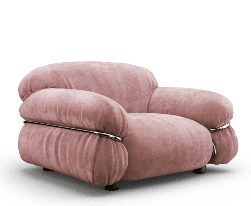 A plush, overstuffed armchair upholstered in a soft, rose-pink velvet-like fabric. The armchair features voluminous, rounded cushions for the seat, back, and arms. Chrome-plated metal tubes are integrated into the design, wrapping around the armrests and supporting the overall structure, adding a contemporary accent to the soft form. It rests on short, dark-colored legs. — 3D model