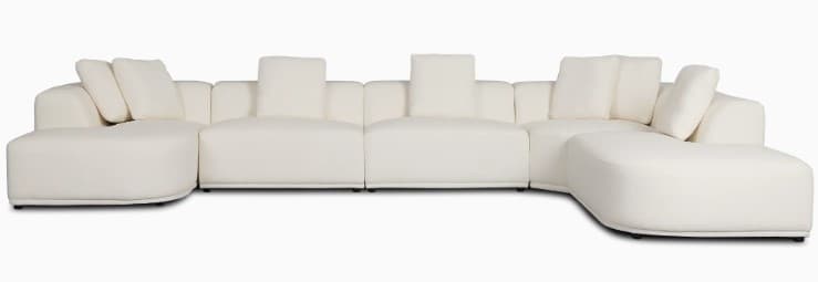 A large, contemporary modular U-shaped sectional sofa upholstered in a cream-colored fabric, featuring soft, rounded edges and a low-profile design, complete with multiple back cushions. — 3D model