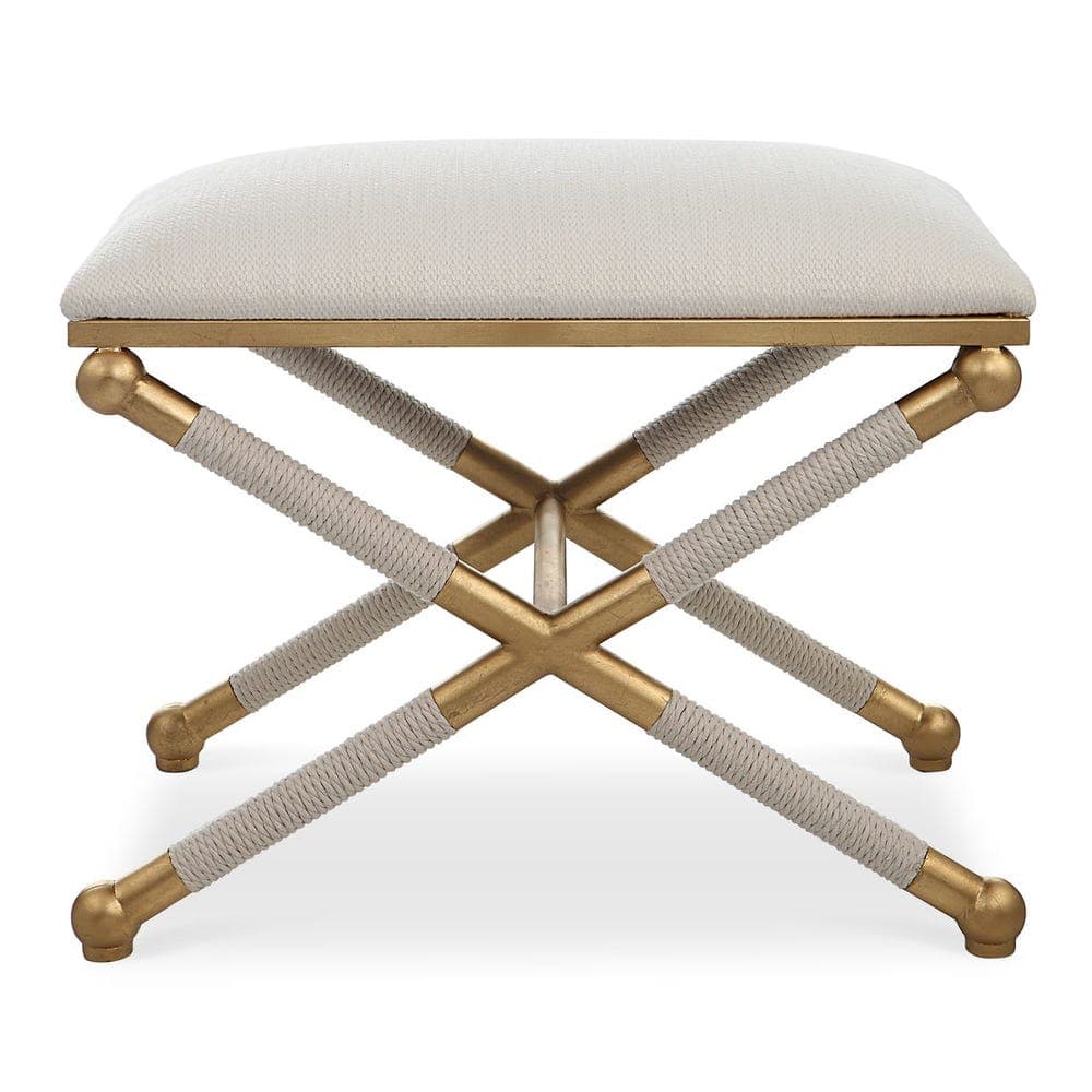 A compact, rectangular upholstered ottoman featuring a distinctive X-shaped metallic base partially wrapped in rope. The cushioned seat is covered in a light, textured fabric, resting on a gold-finished frame with decorative spherical feet. — 3D model