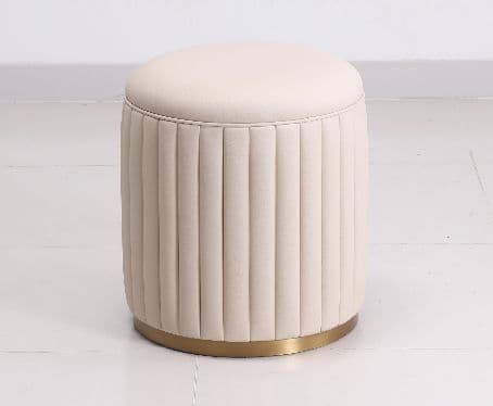 A modern, cylindrical upholstered ottoman featuring vertical fluting around its body and a smoothly padded, flat top. It rests on a polished brass-toned metallic base, presenting a luxurious and contemporary aesthetic. — 3D model