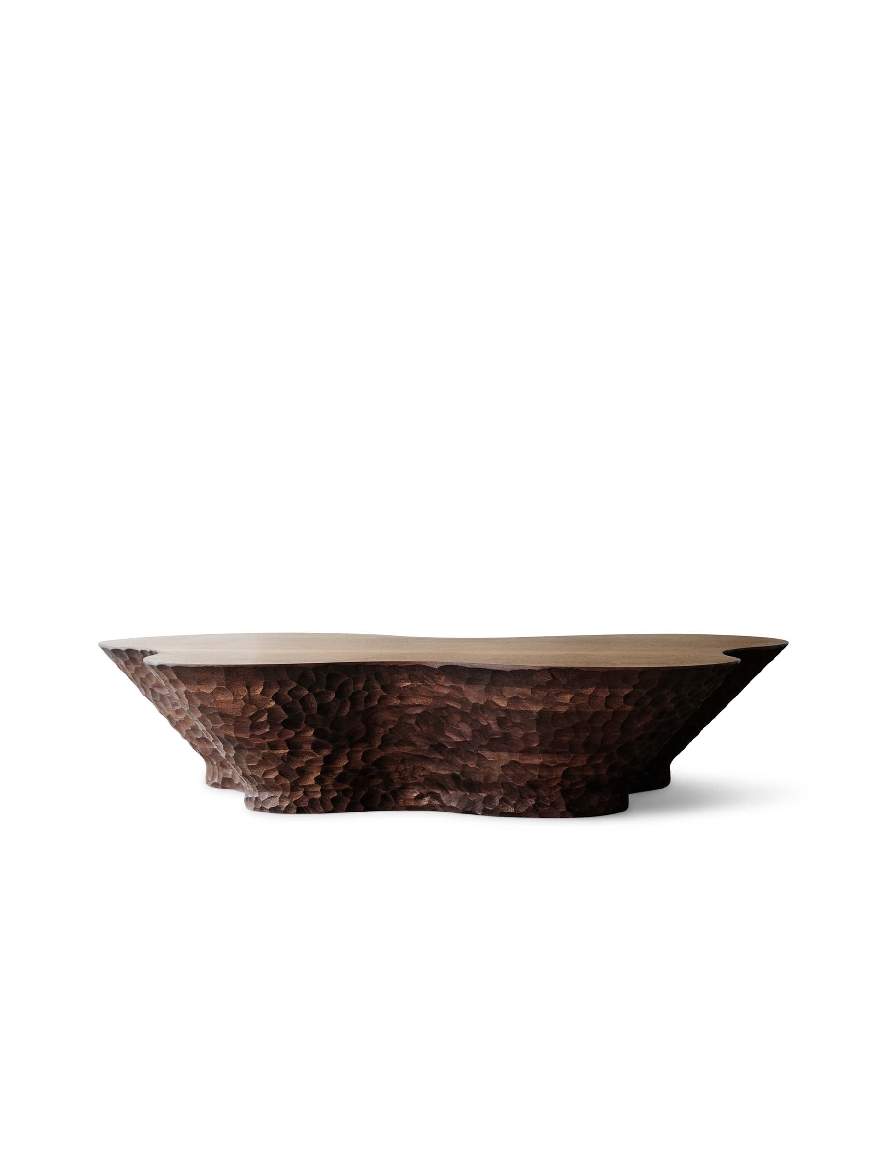A low, wide coffee table made of dark wood, featuring a smooth top surface and highly textured, hand-carved sides and base. The shape is organic and irregular, resembling a natural formation with a rugged, chiseled aesthetic. — 3D model