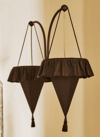 An arched floor lamp featuring two suspended cone-shaped fabric shades. The lamp has a dark brown or bronze-finished metal frame with two distinct arched arms. Each arm supports a fabric shade, which is ruffled at the top and tapers downwards into a conical form, ending with a decorative tassel. The overall aesthetic combines modern structural elements with traditional or eclectic textile details. — 3D model