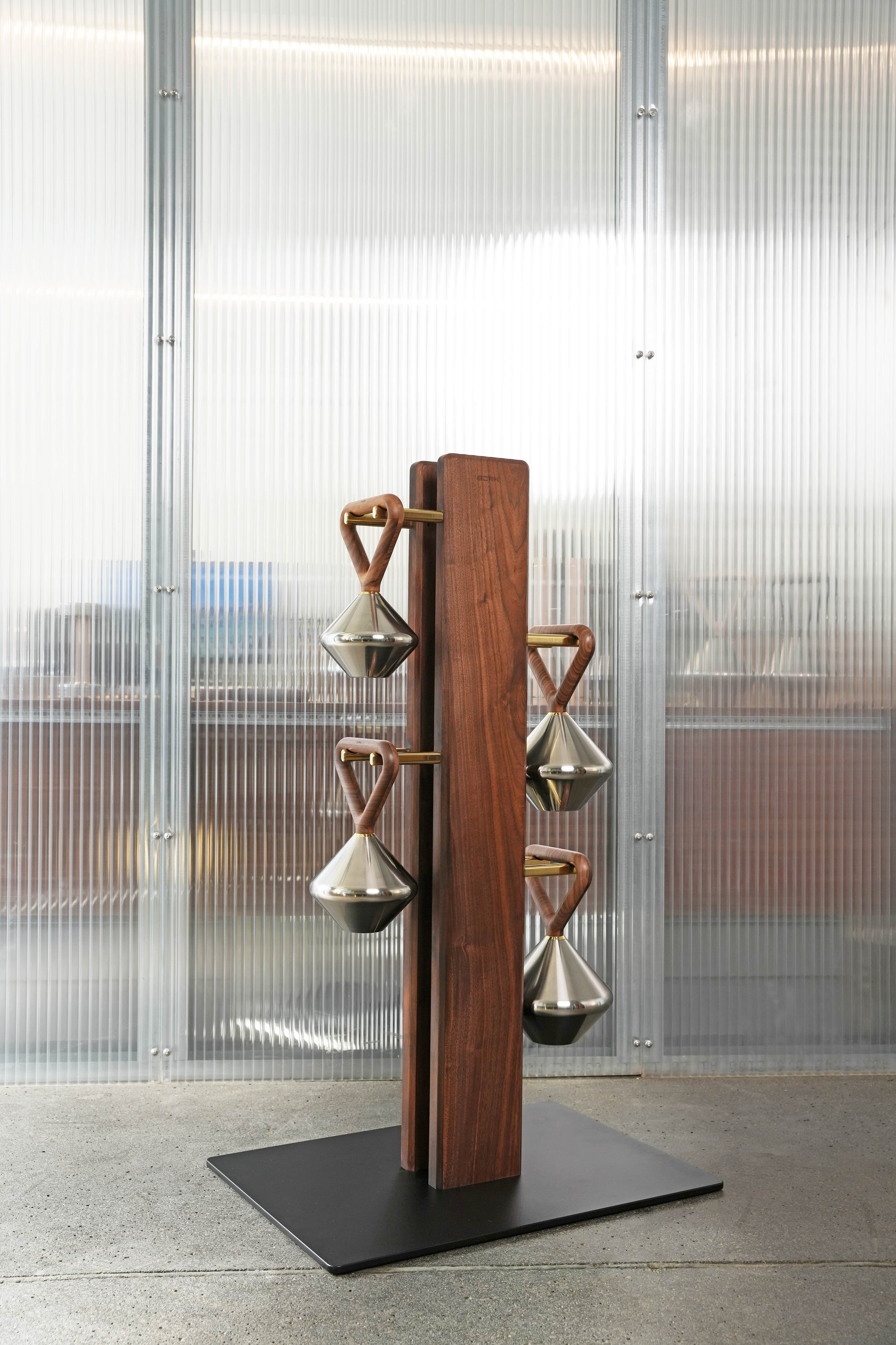 A modern freestanding coat rack featuring two vertical walnut wood columns, from which six conical p… — 3D model
