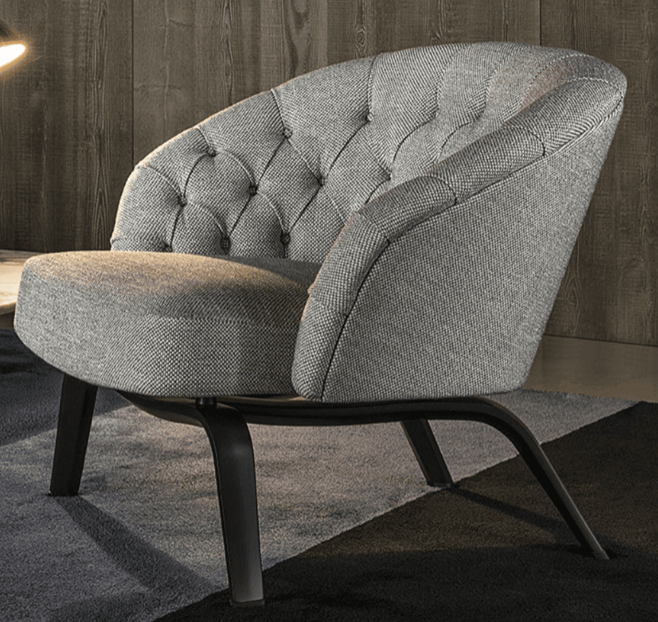 A modern armchair with a rounded, tufted backrest and a comfortably padded seat. The chair features a low profile and is supported by dark, slender legs with a curved design. The upholstery has a textured appearance. — 3D model