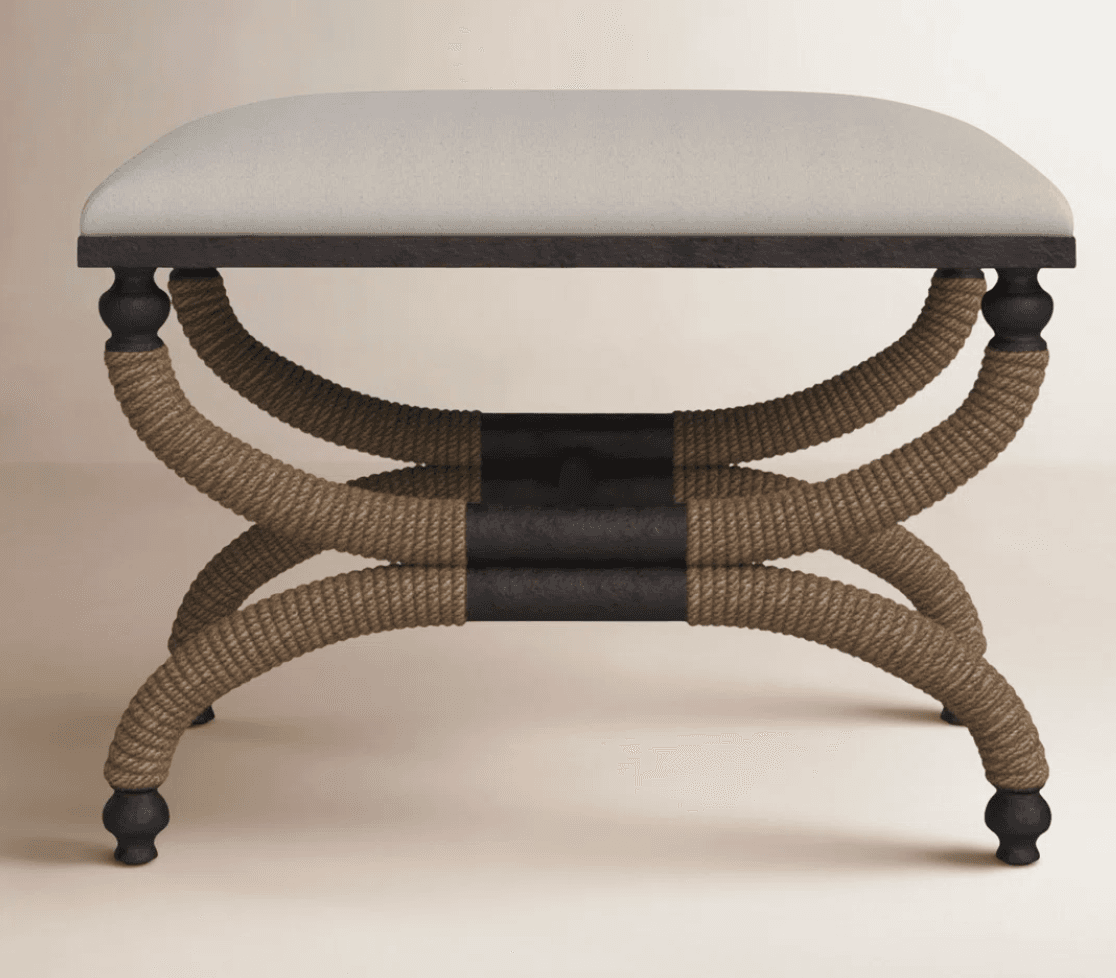 A stool with a cushioned top and a decorative base. The base features four legs made of dark-colored material, possibly wood or metal, connected by curved supports. These supports are wrapped with thick, braided rope in a natural tan color, forming an 'X' shape between the legs. The overall design suggests a blend of classic and coastal aesthetics. — 3D model