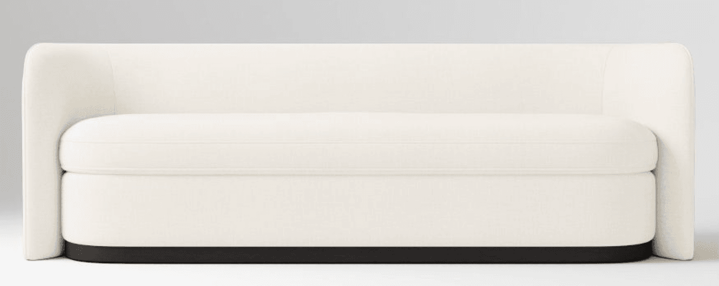 A contemporary loveseat upholstered in a light, off-white fabric, featuring a minimalist design. It has integrated high armrests and a high back that form a continuous, enveloping shape. The seat consists of two plush, removable cushions. The entire piece rests on a dark, recessed plinth base, giving it a slightly floating appearance. — 3D model