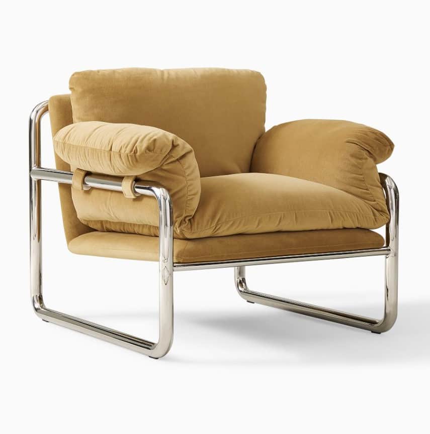 A modern armchair featuring a polished chrome tubular frame with large, plush, camel-colored fabric… — 3D model